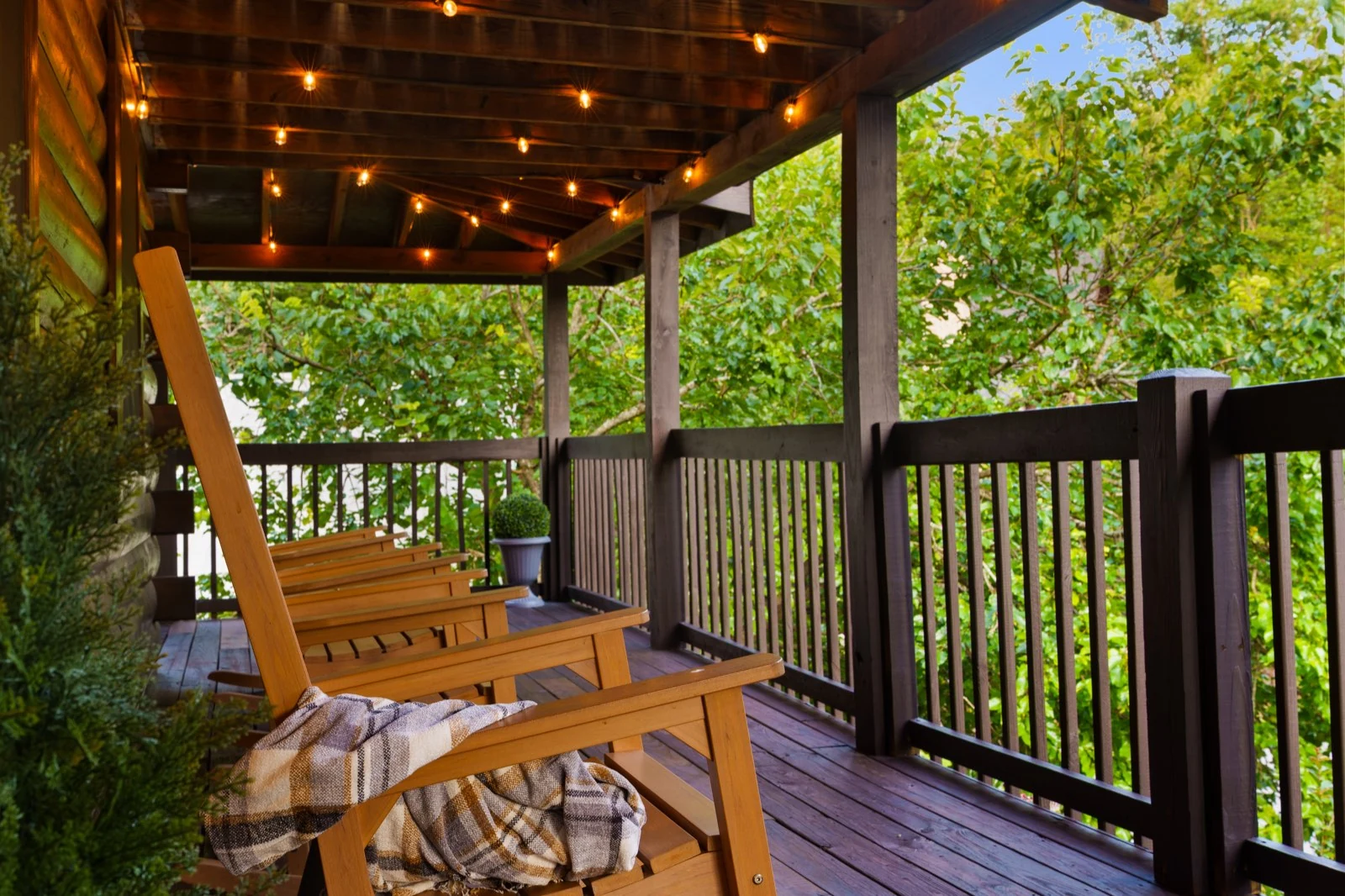 Rocking chairs and a soft throw beneath string lights on the wooded deck